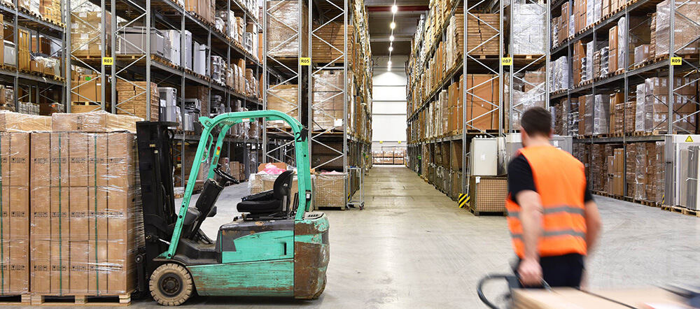 倉庫内でフォークリフトがパレットを運搬し、作業員が荷物を引いている様子